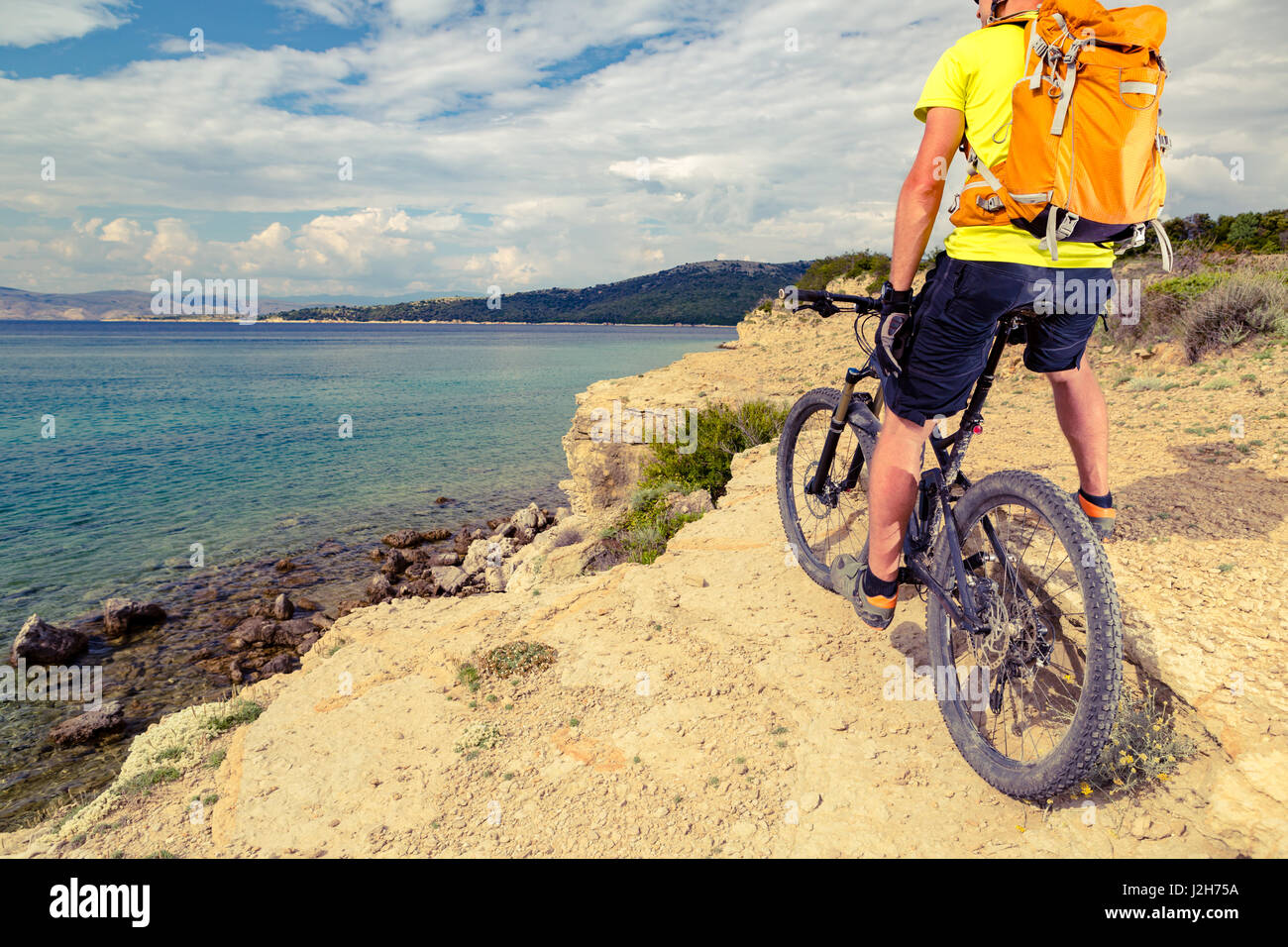 Mountain biker looking at view and traveling on bike in summer sea landscape. Man rider cycling MTB on rocky yellow trail. Fitness motivation, inspira Stock Photo