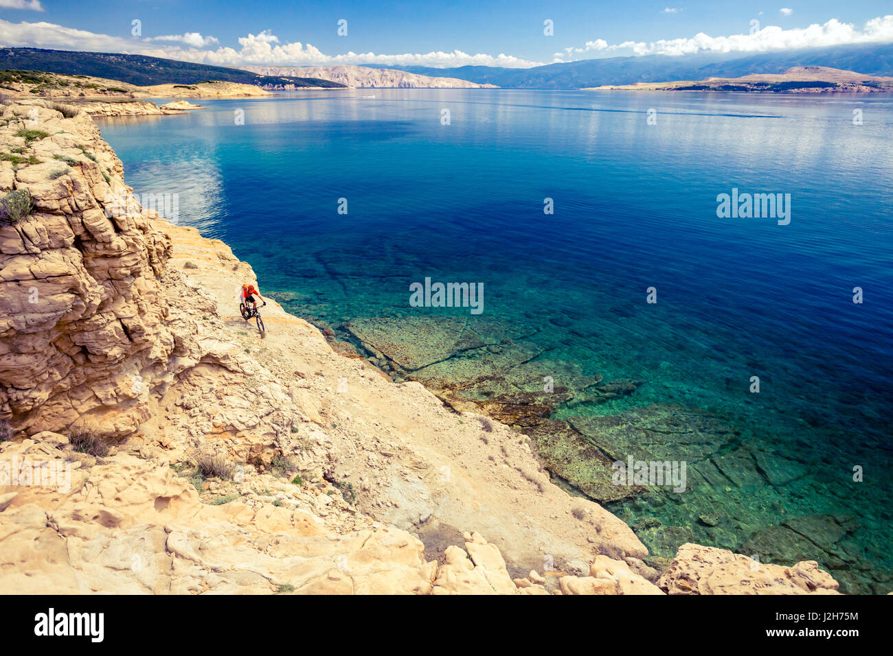 Mountain biker riding on bike in summer inspirational mountains and sea landscape. Man cycling MTB on enduro trail track at seaside and rocky dirt pat Stock Photo