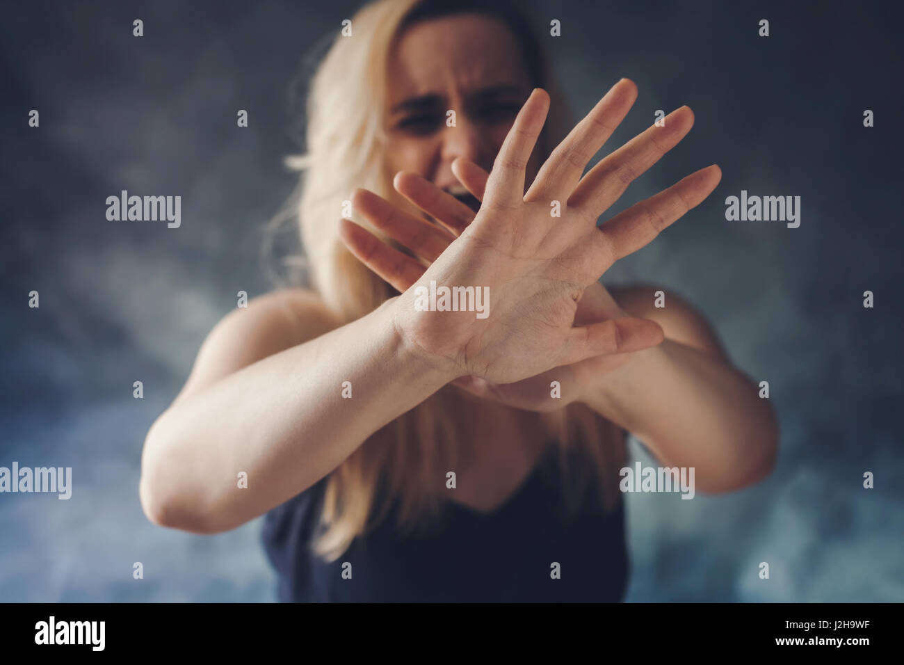 Woman screaming in fear, defending herself with hands in front of her face Stock Photo