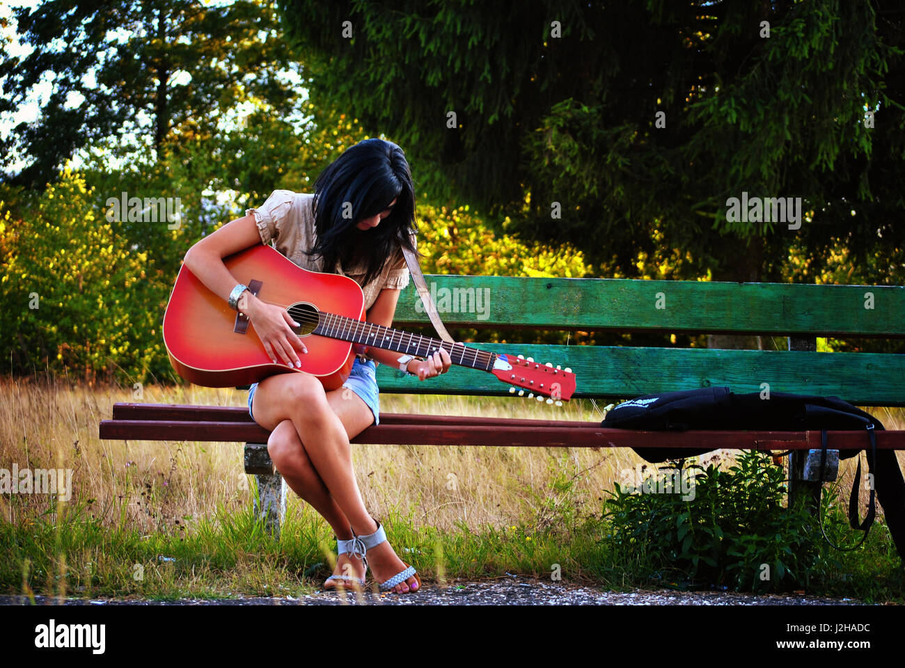 Young girl playing guitar on a bench outside Stock Photo - Alamy