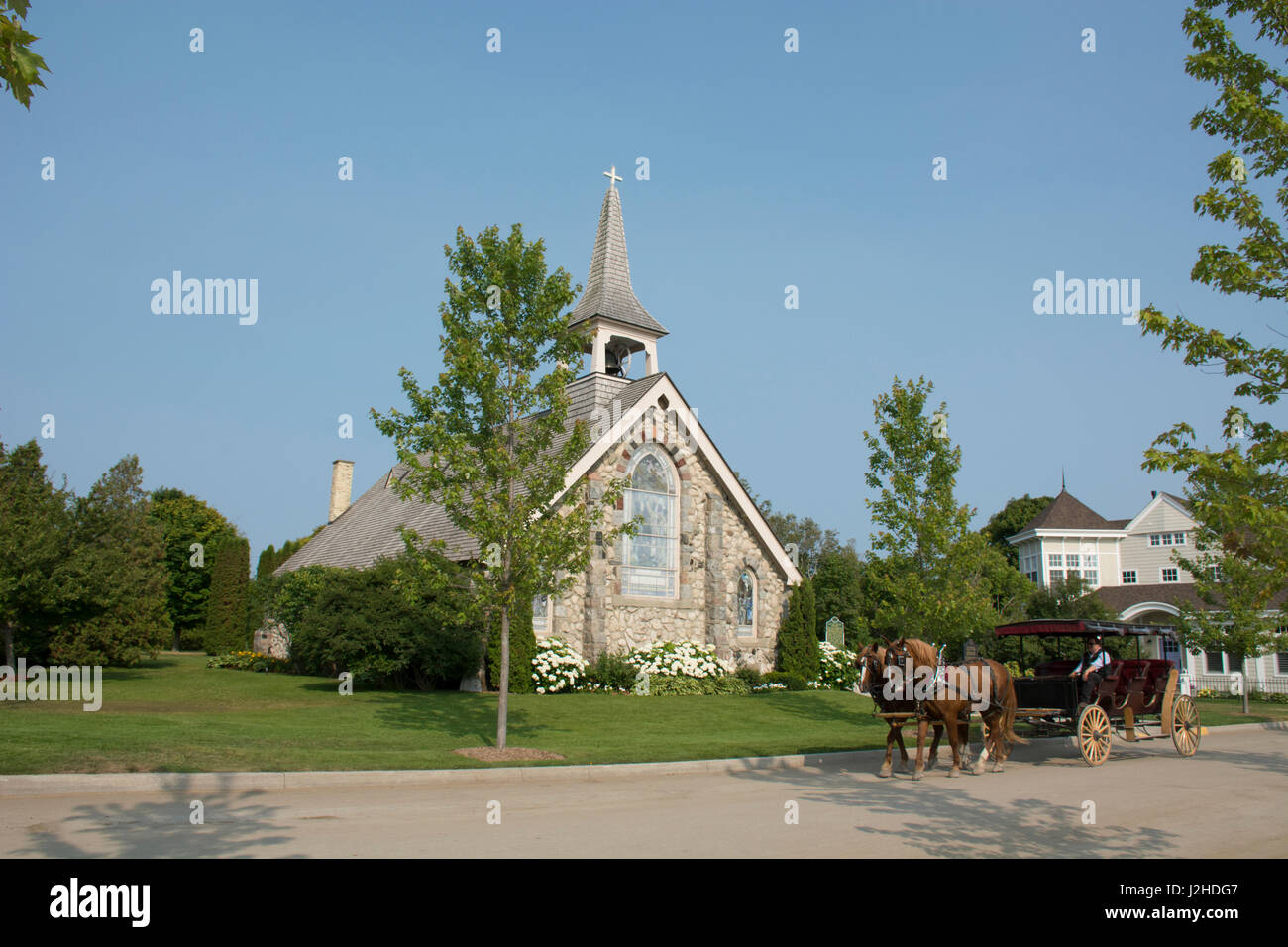 Michigan, Mackinac Island. Scenic horse carriage ride past the Little Stone Church. Stock Photo