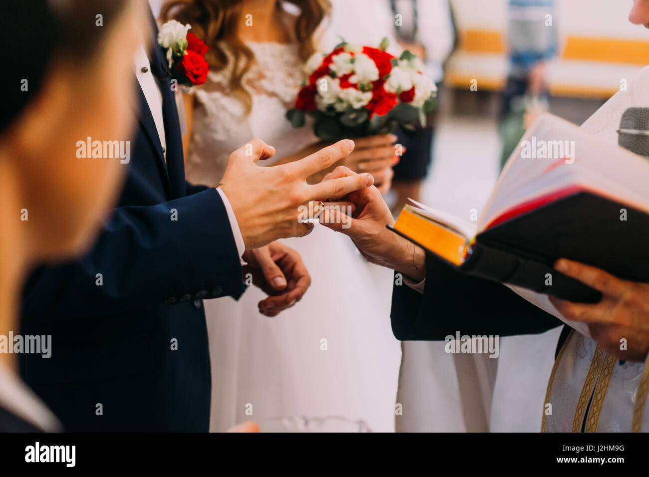 Priest putting golden ring on a bridegroom hand at wedding ceremony in
