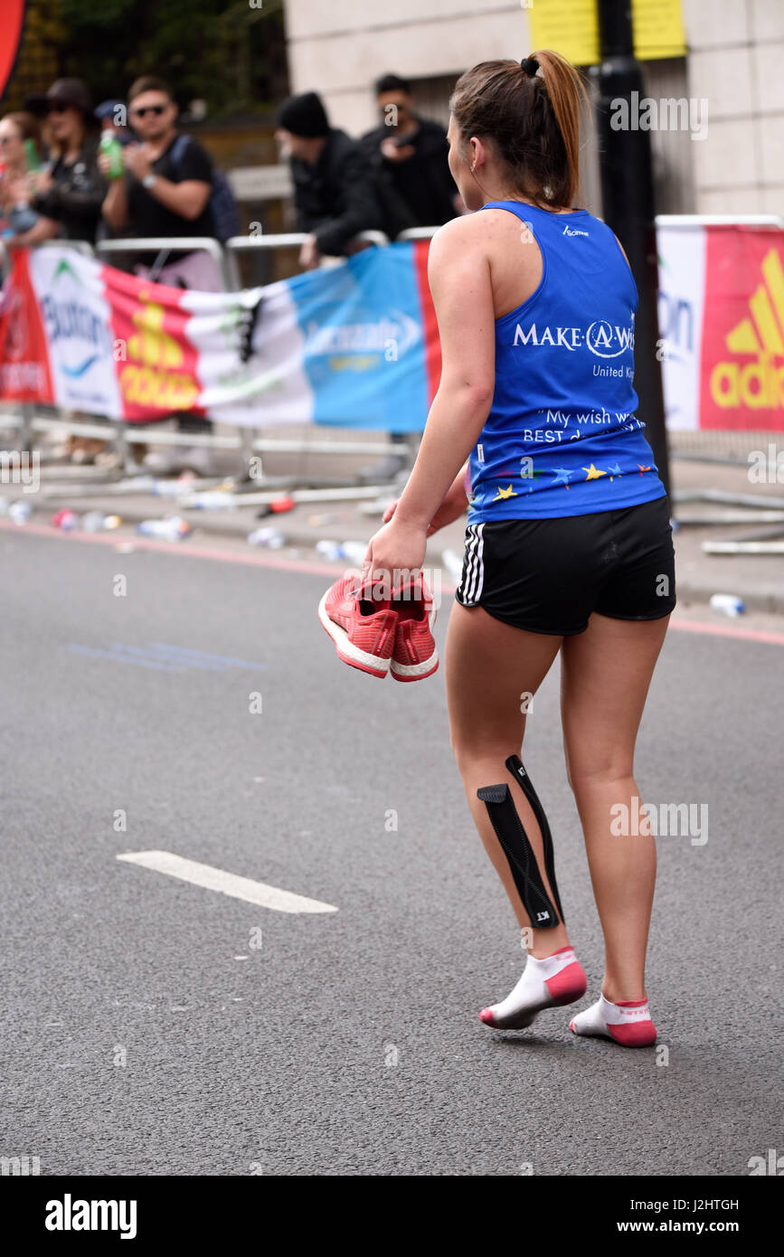 A girl taking part in the 2017 London Marathon carrying her running shoes, with support tape Stock Photo