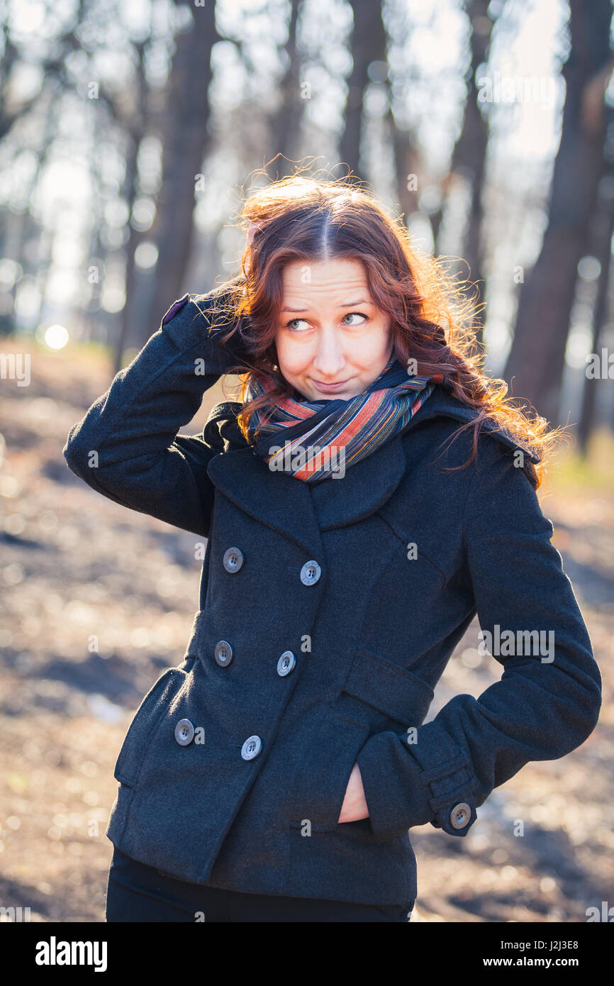 Smiling red-haired girl outdoors, weared coat and scarf. Early spring in park ar sunset. Stock Photo