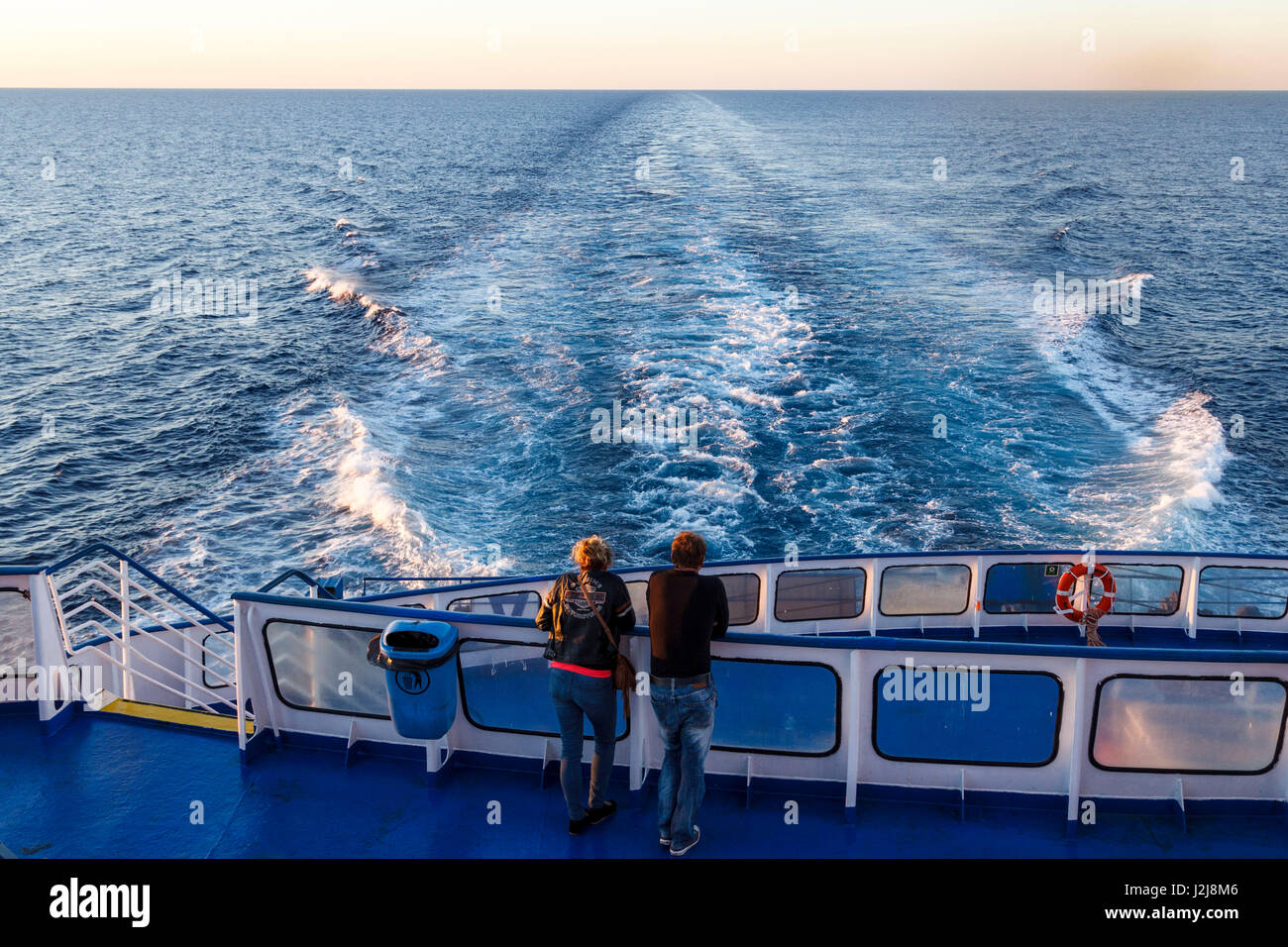 A man and a woman stand on the stern of a ship and watch the sunrise ...