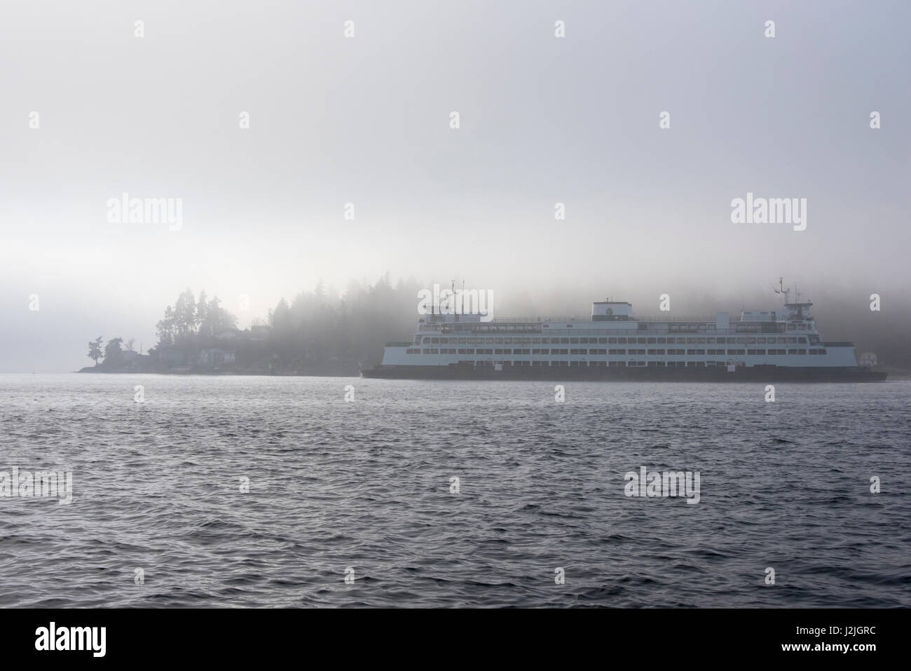 USA, Washington State, Puget Sound. Ferry emerges Rich Passage from dense fog to round Point Glover Stock Photo