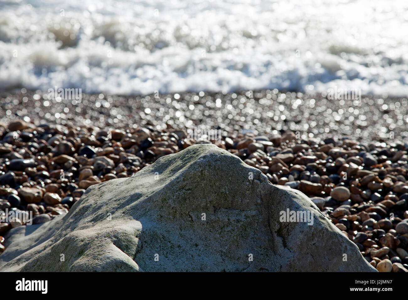 Wintery light falling on a solitary rock on a pebbly beach with the sea beyond Stock Photo