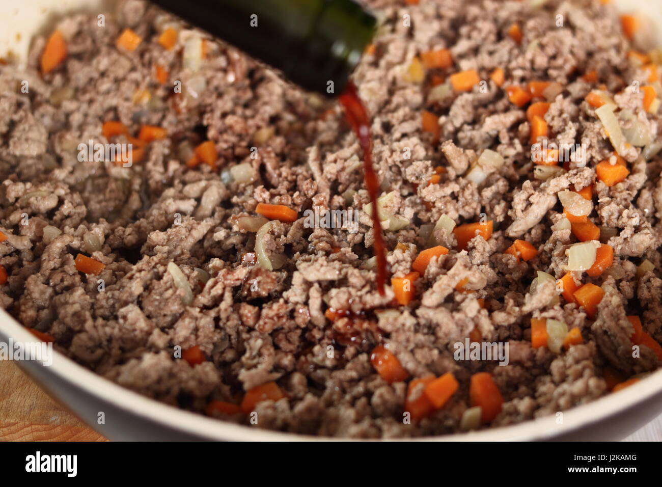 Pouring red wine into minced meat. Making Lasagna Bolognese Series. Stock Photo