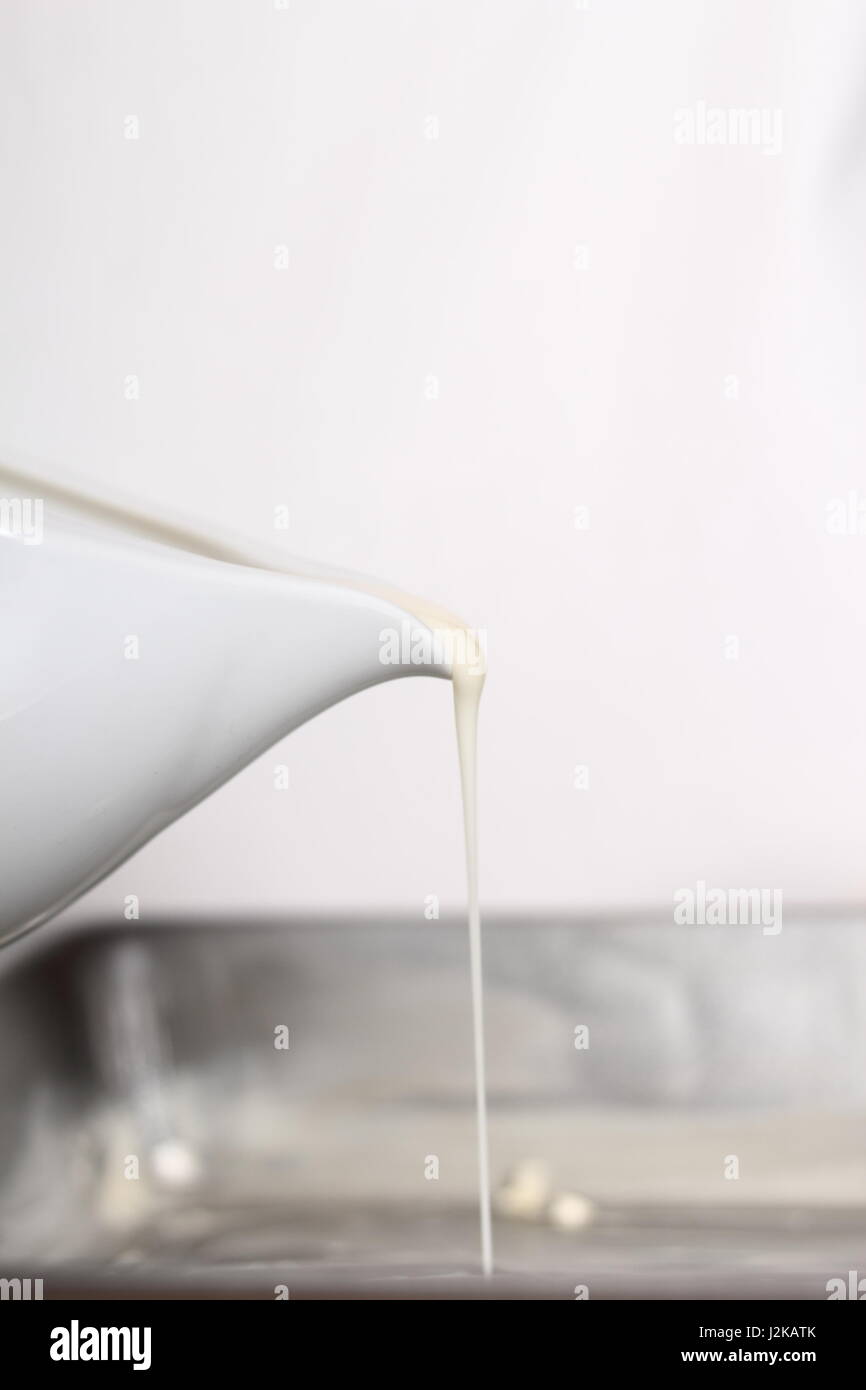 Pouring bechamel sauce using gravy boat into baking pan. Making Lasagna Bolognese Series. Stock Photo