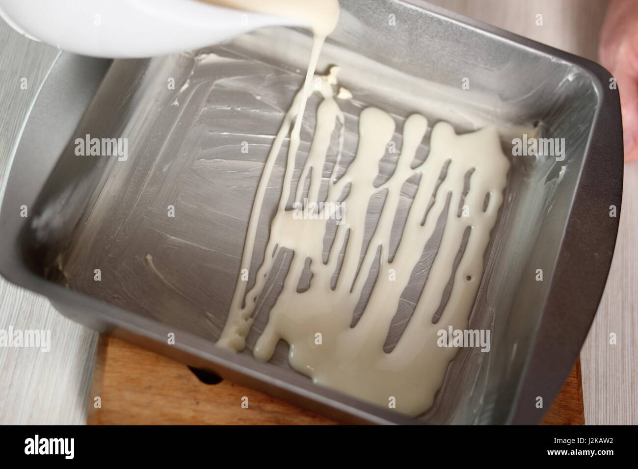 Pouring bechamel sauce using gravy boat into baking pan. Making Lasagna Bolognese Series. Stock Photo