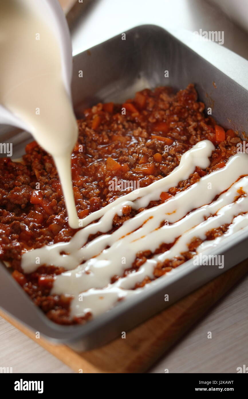 Pouring bechamel sauce onto ground meat layer. Making Lasagna Bolognese Series. Stock Photo