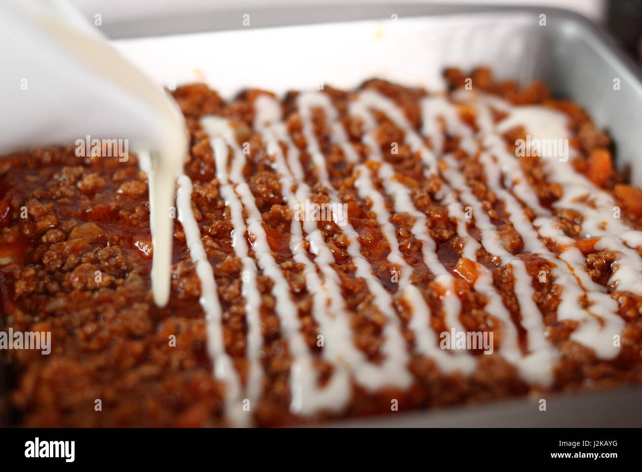 Pouring bechamel sauce onto ground meat layer. Making Lasagna Bolognese Series. Stock Photo