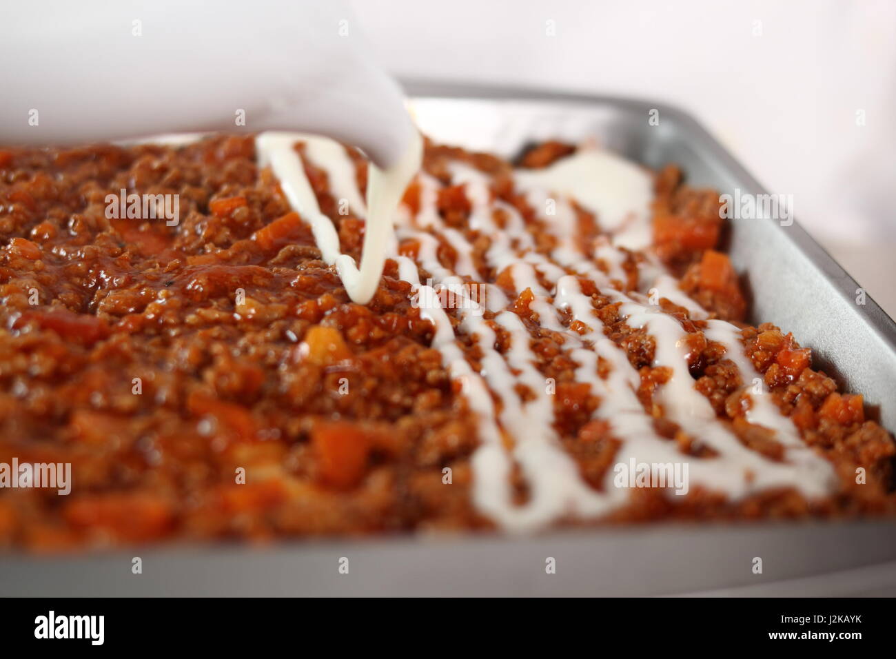 Pouring bechamel sauce onto ground meat layer. Making Lasagna Bolognese Series. Stock Photo