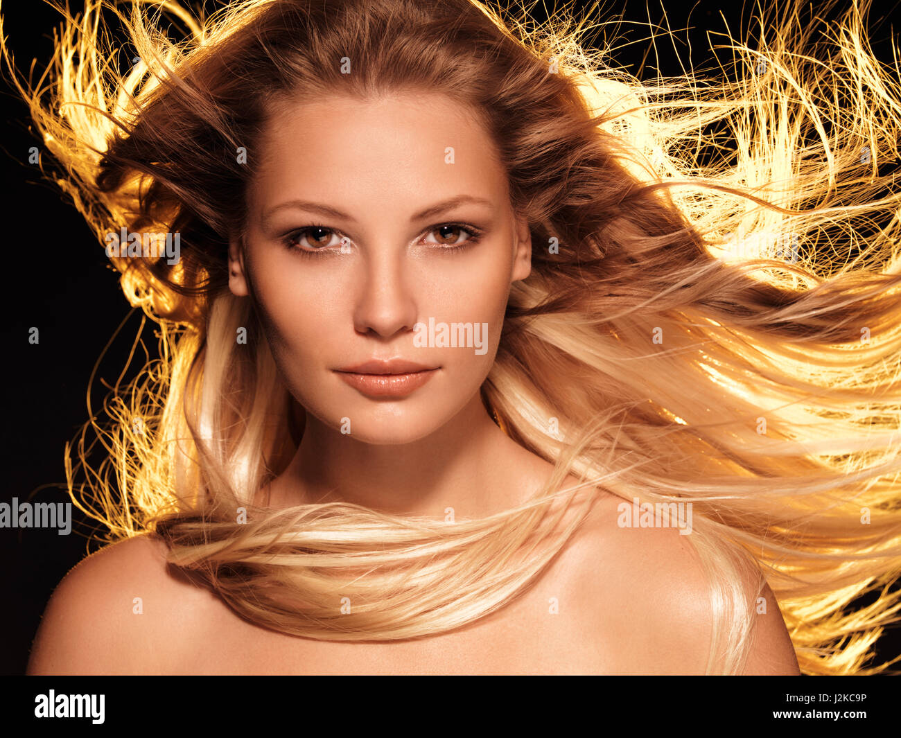 License and prints at MaximImages.com - Beauty face portrait of a woman with long glowing flying golden blond hair front view Stock Photo