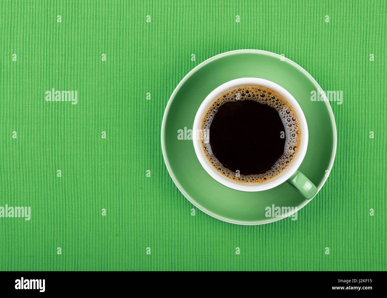 Full cup of black Americano or instant coffee on saucer over green tablecloth, close up, elevated top view Stock Photo