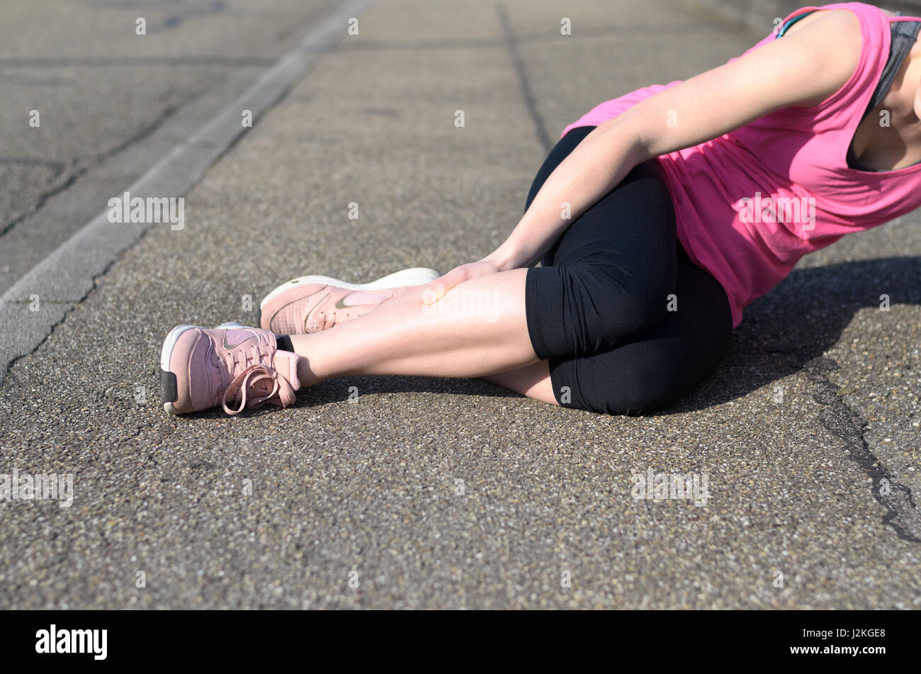 Female athlete with calf cramps lying on the sidewalk of a tarred road