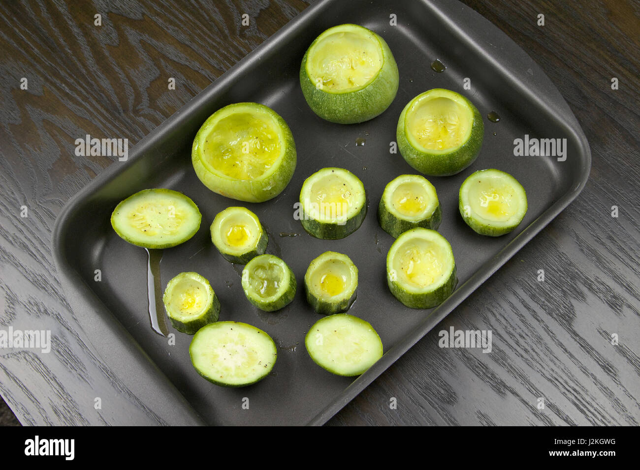 Emptied zucchini (courgette) in a baking tin lying on a dark wooden table - Preparing stuffed zucchini recipe Stock Photo