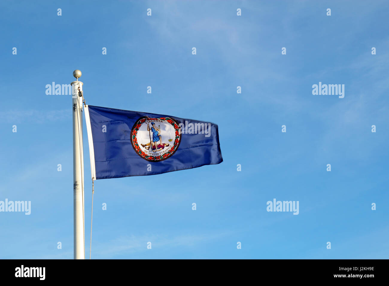 Flag of the Commonwealth of Virginia flying from a while pole against a bright blue sky and cirrus clouds background Stock Photo