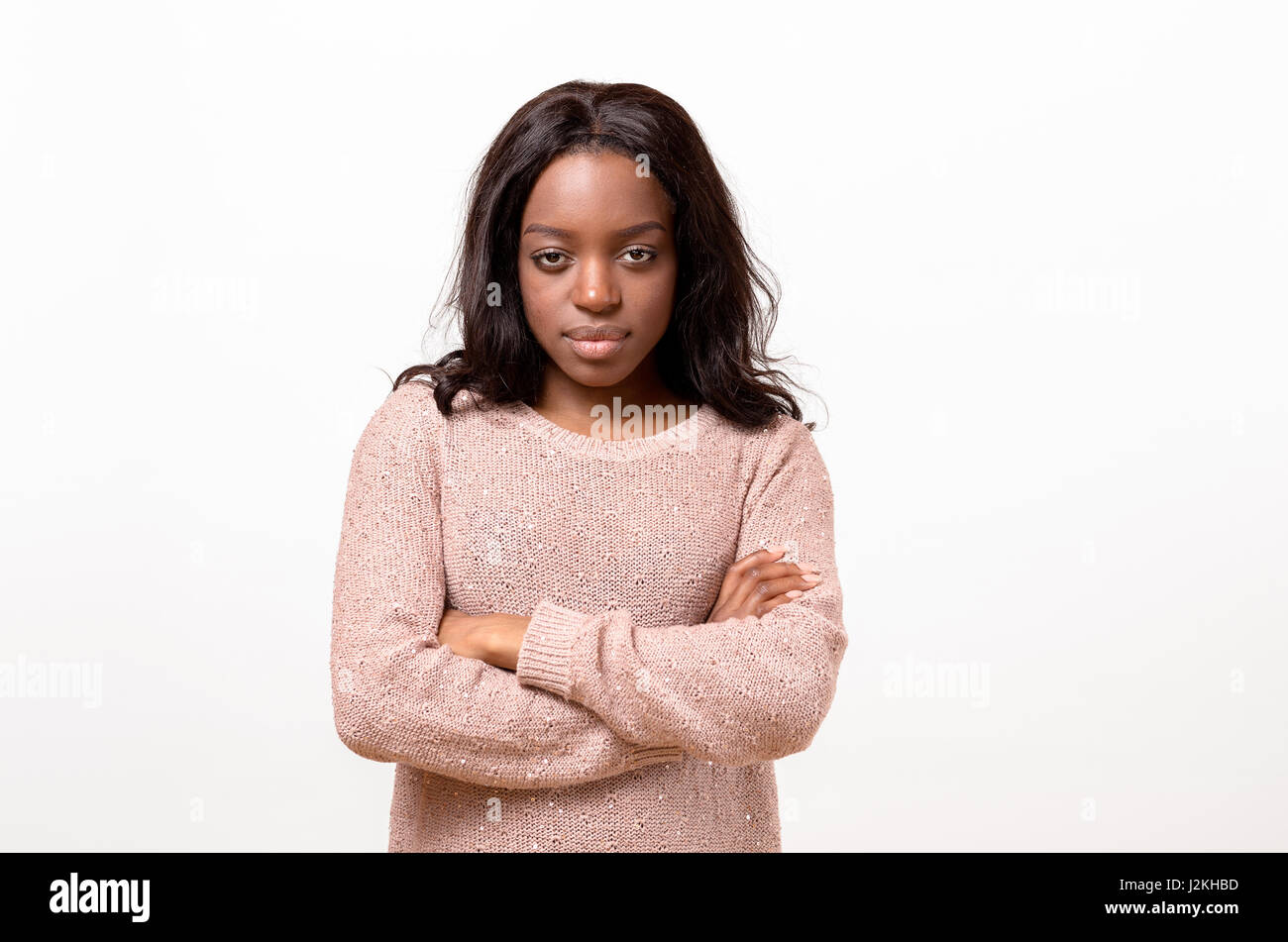 Serious young African American woman standing with folded arms staring at the camera with a calm emotionless expression isolated on white Stock Photo