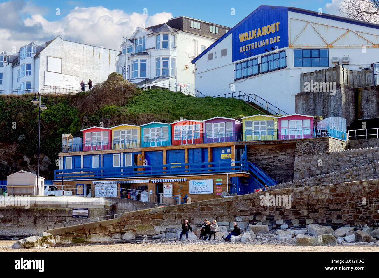 Newquay, Cornwall, UK - April 1 2017: Colourful beach huts above Newquay beach, in front of the Walkabout Australian Bar - unidentified people enjoy t Stock Photo