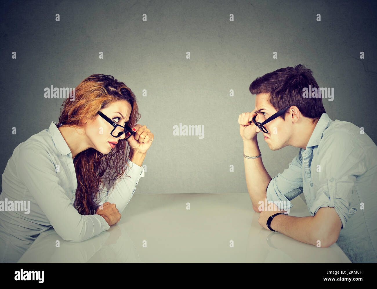 Angry man and woman sitting at table looking at each other with hatred and disgust Stock Photo