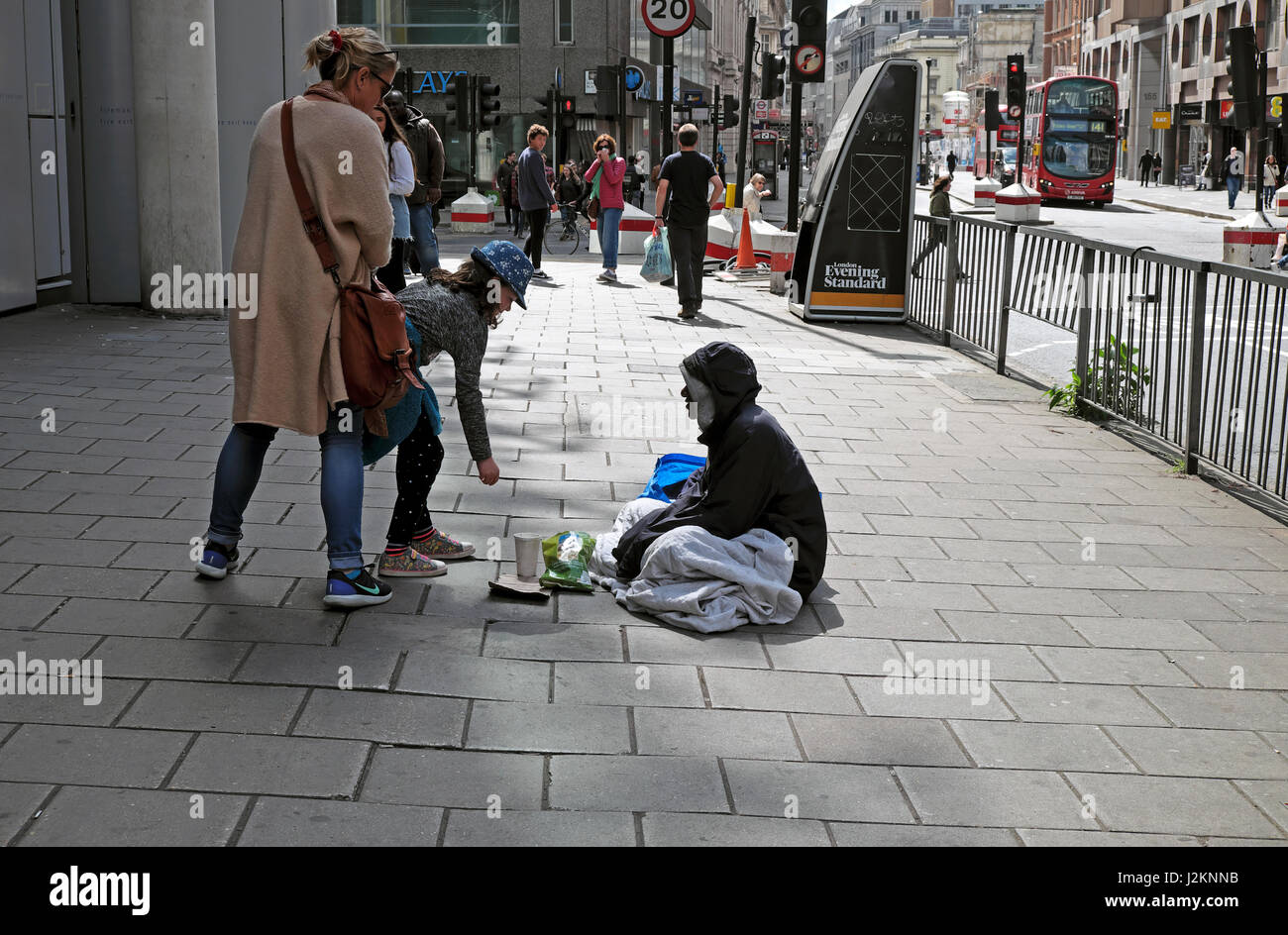 A kind girl talking to putting money coins into the cup of poor homeless man sitting  begging on street with cup in City of London UK  KATHY DEWITT Stock Photo
