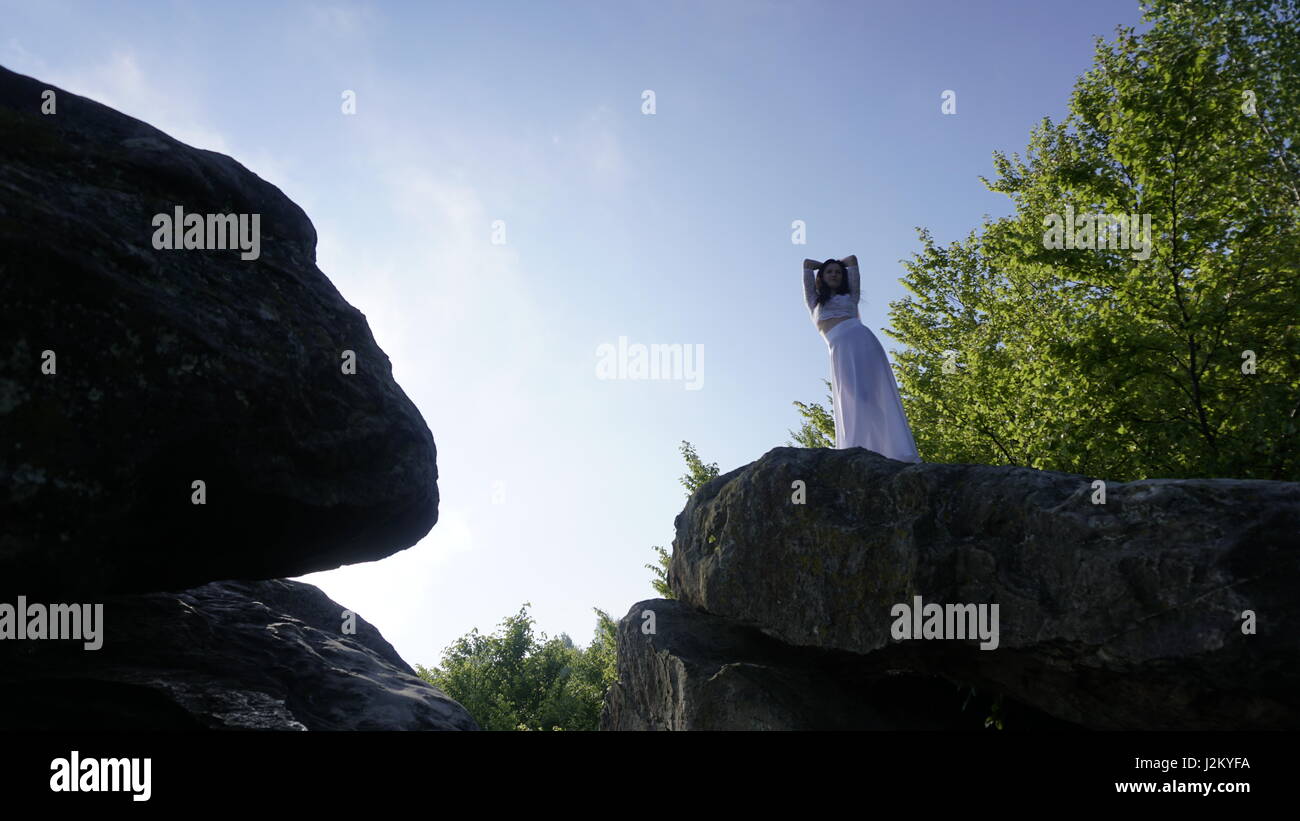 Young bride in wedding dress standing on the rock and posing for camera ...