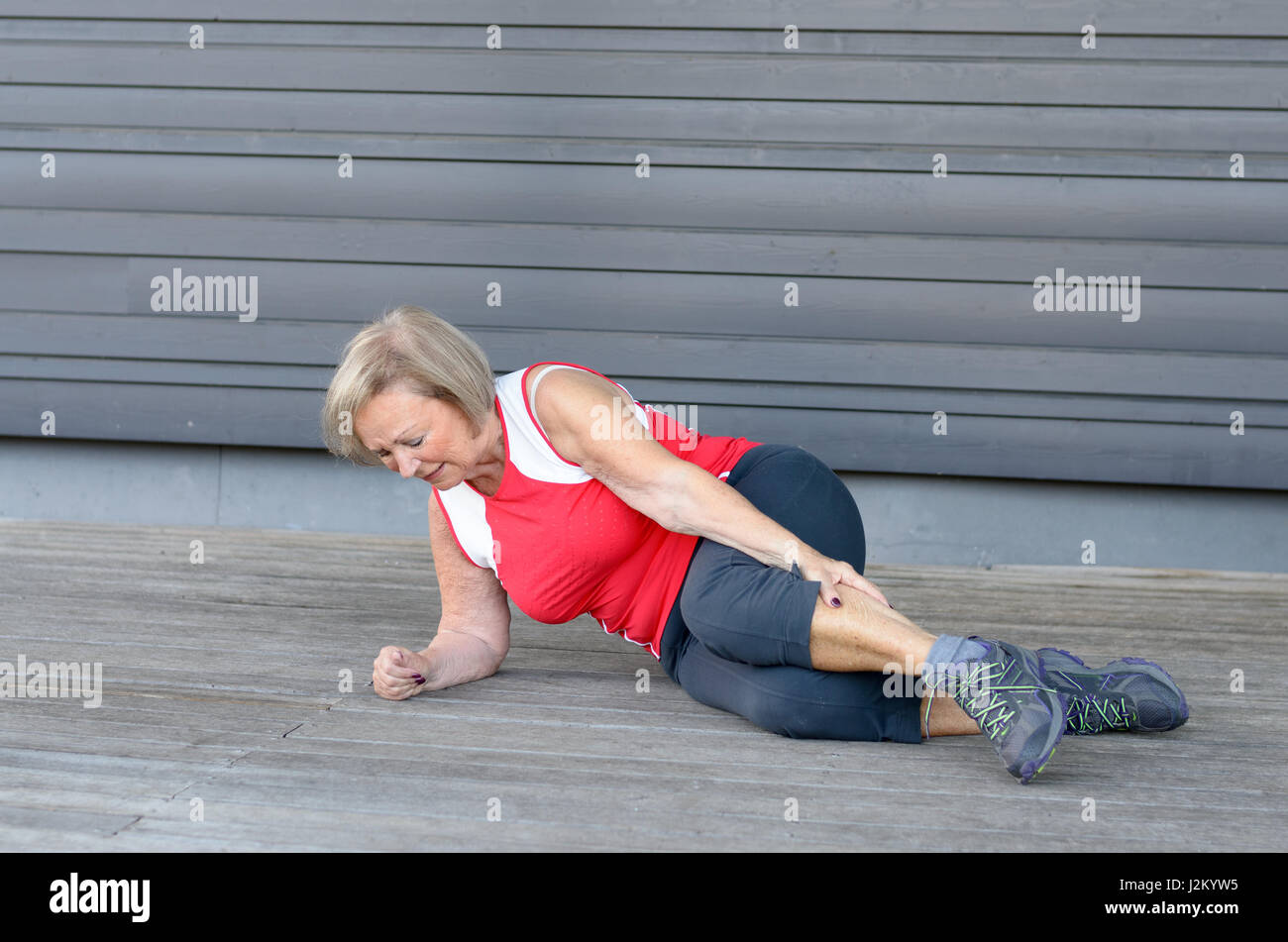 Senior woman with severe muscle cramps in her calf clutching her lower leg in pain as she lies on the floor during a sports workout Stock Photo