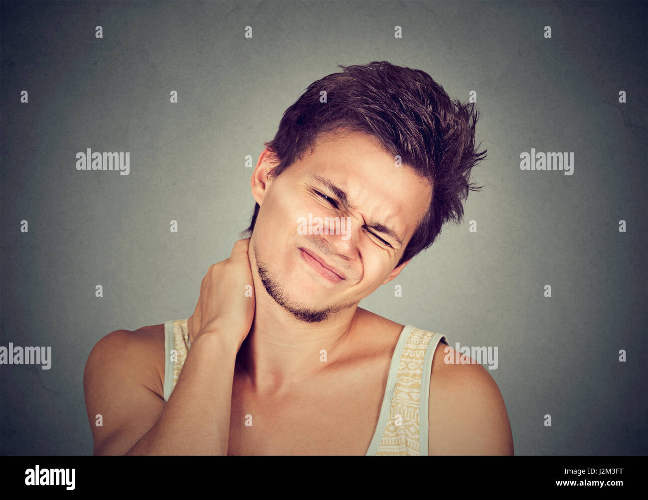 Stressed young handsome man with neck pain isolated on gray wall background. Negative human emotion facial expression Stock Photo