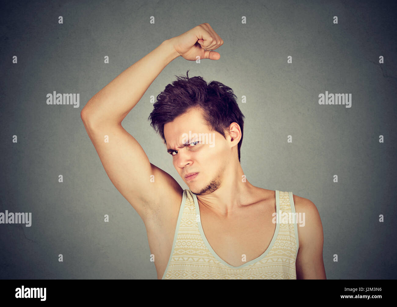 Closeup portrait of young man, smelling, sniffing his armpit, something stinks, very bad, foul odor situation, isolated on gray wall background. Negat Stock Photo