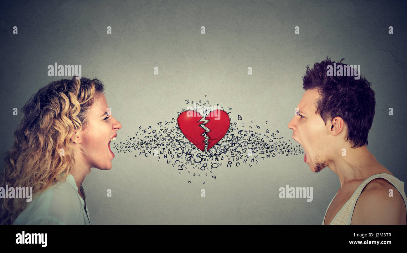 Side profile young man and woman screaming at each other with alphabet letters coming from mouth and broken heart in-between isolated on gray wall bac Stock Photo