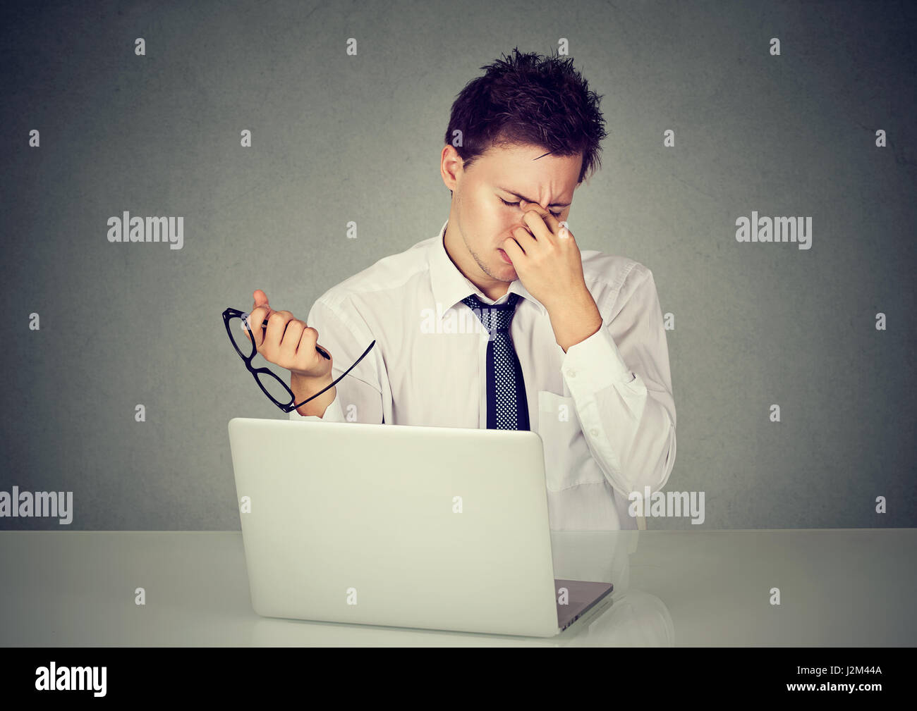 Young tired business man rubbing his eye sitting at table in front of laptop in his office Stock Photo