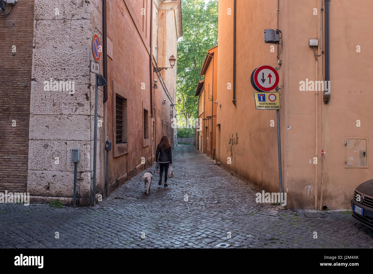 Woman walking a dog down a narrow Italian street. Stock Photo