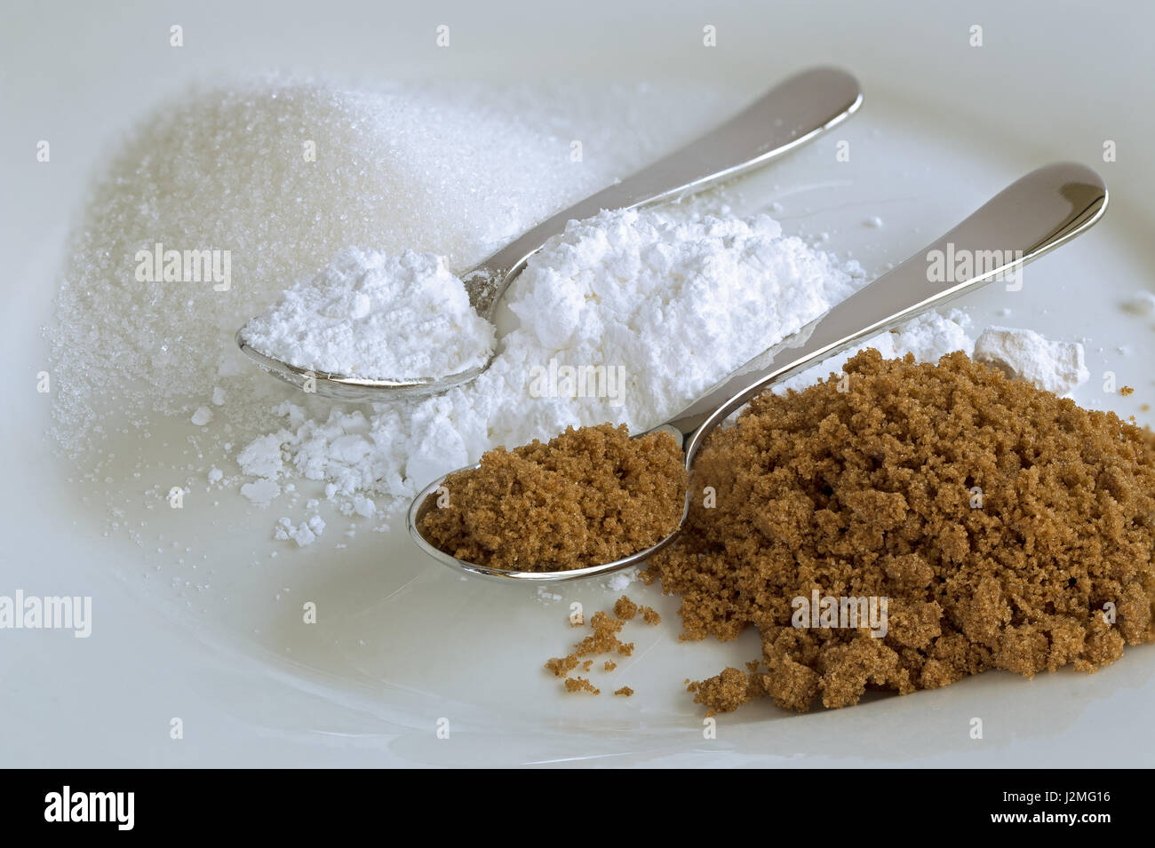 Two shiny spoons on small heaps of brown, icing and granulated sugar on
