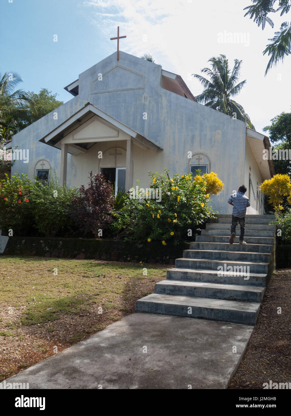 TODAK ISLAND, BATAM, INDONESIA. A boy steps up the stairs in front of a white wall church. Stock Photo
