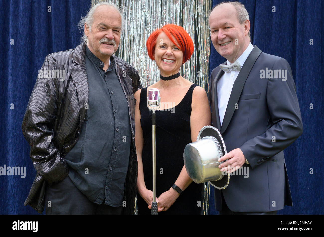 Three lively performers on stage celebrating in front of a microphone with a vivacious redhead woman and two gentlemen with top hats laughing and joki Stock Photo