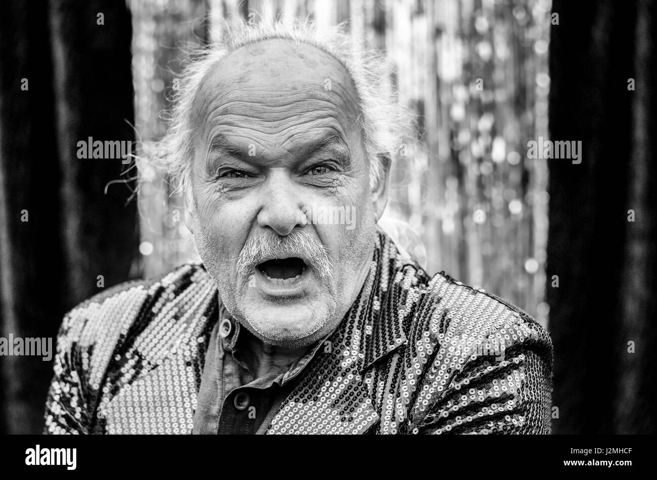 Infuriated elderly man shouting at the camera with an angry expression and baleful stare in a head and shoulders toned greyscale image Stock Photo