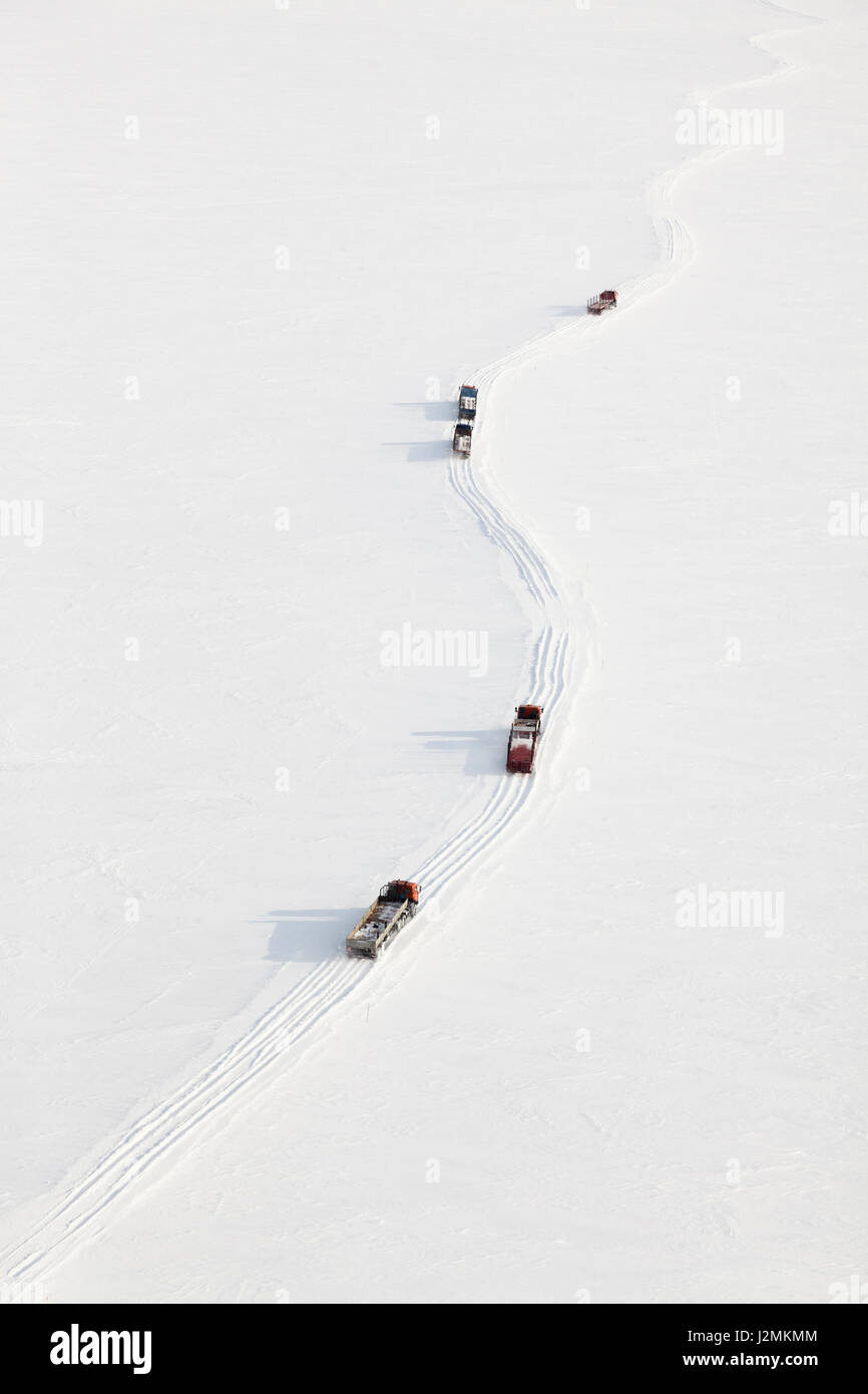 Trucks moving through out road in the snow covered tundra in vicinity of oil field, top view. Stock Photo