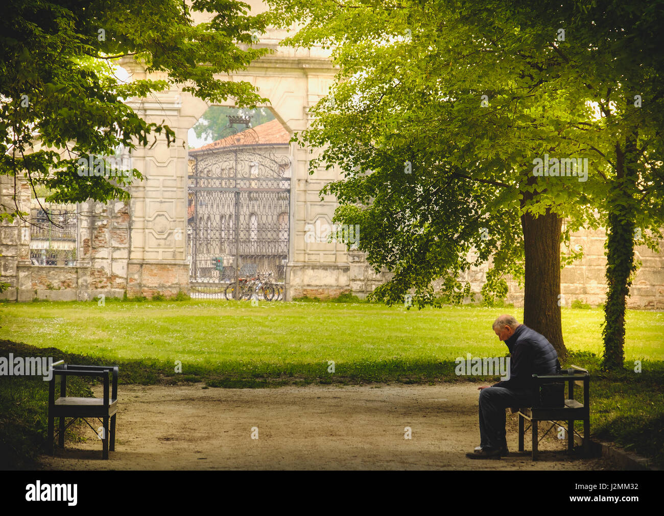 Stra, Italy, 25 Apr 2017 - aged man sitting in loneliness on a park banch in the shade of trees Stock Photo