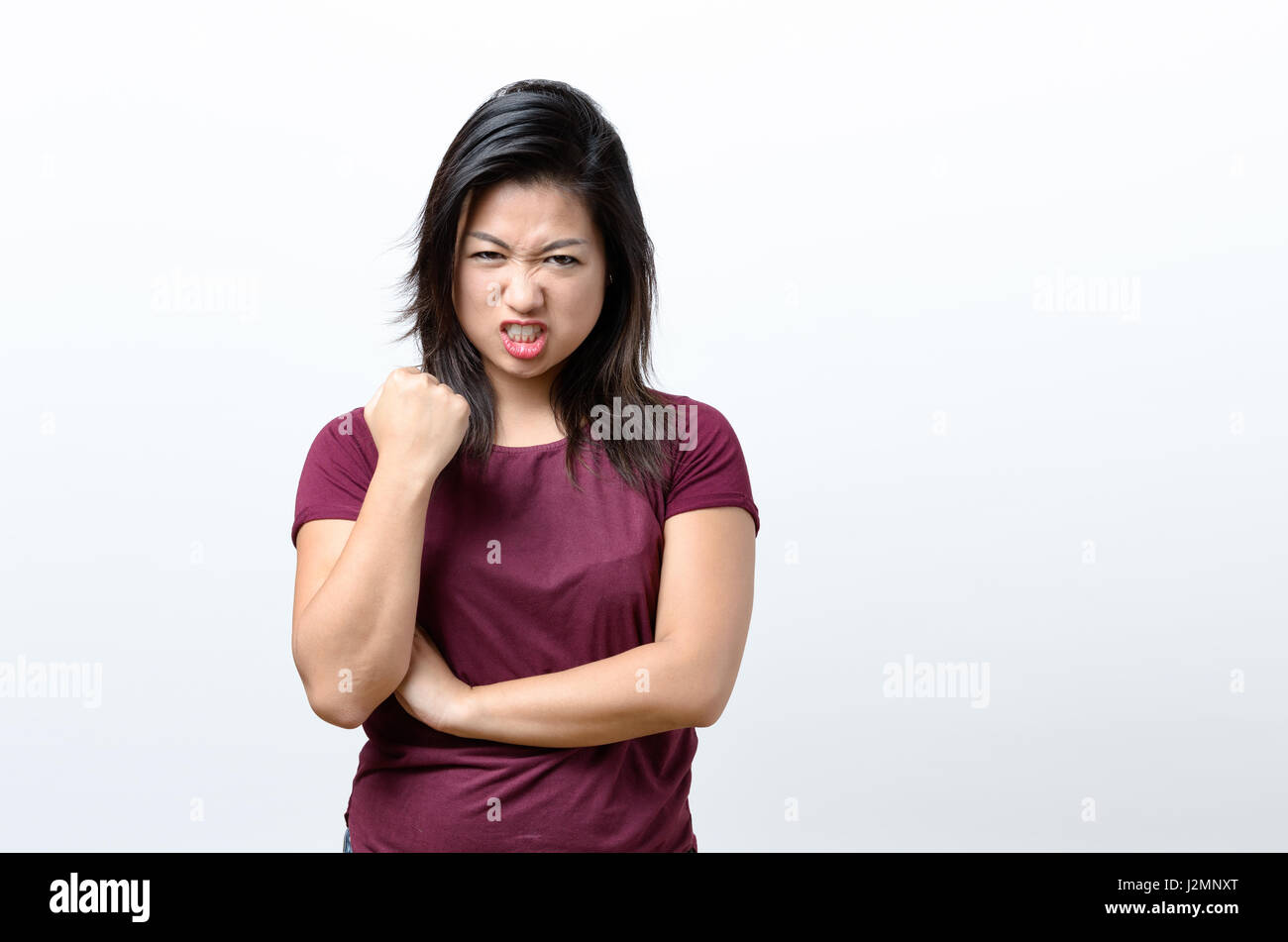 Angry young Chinese woman standing snarling at the camera and shaking her fist with a baleful glare over white with copy space Stock Photo