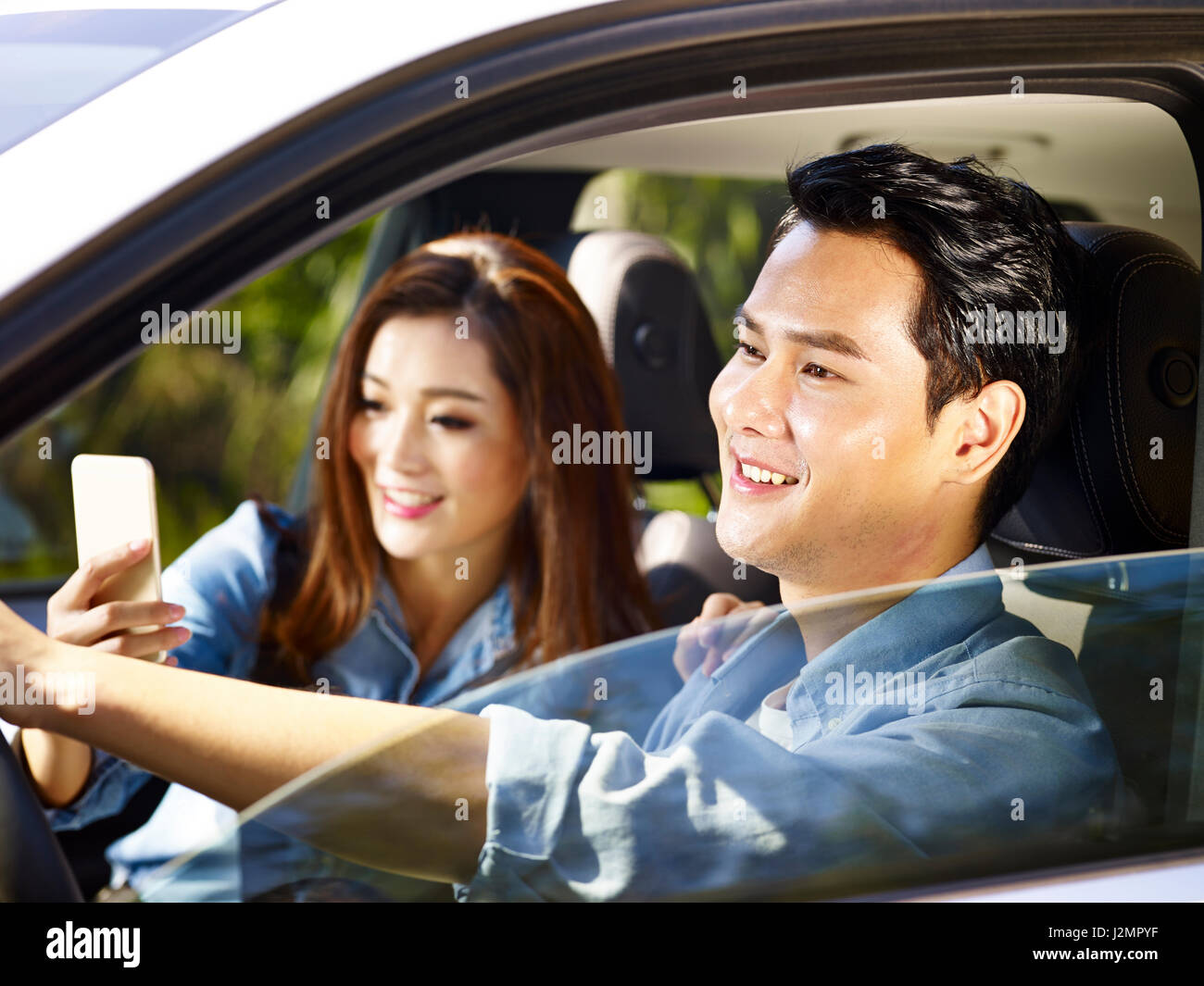 young asian couple enjoying ride in a car, woman taking a selfie. Stock Photo