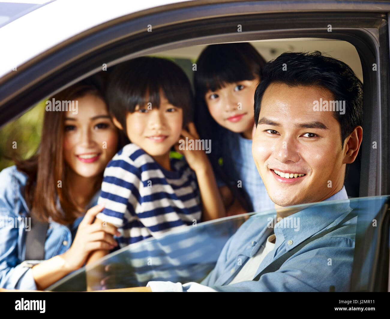 happy asian family with two children traveling by car, focus on the man. Stock Photo