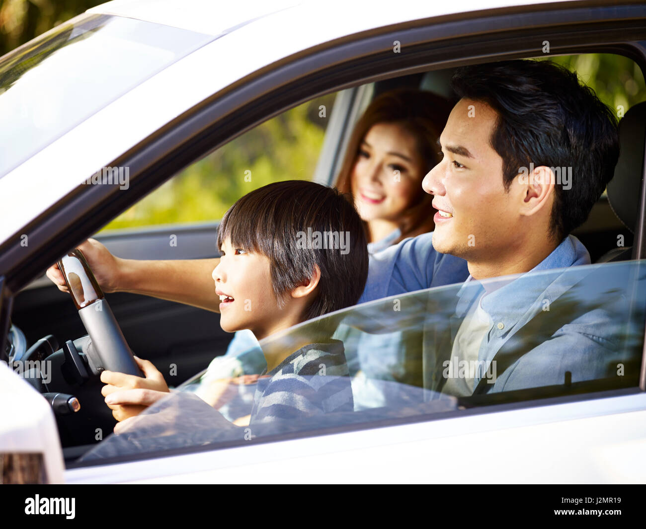 asian father letting his son hold the steering wheel of his car. Stock Photo