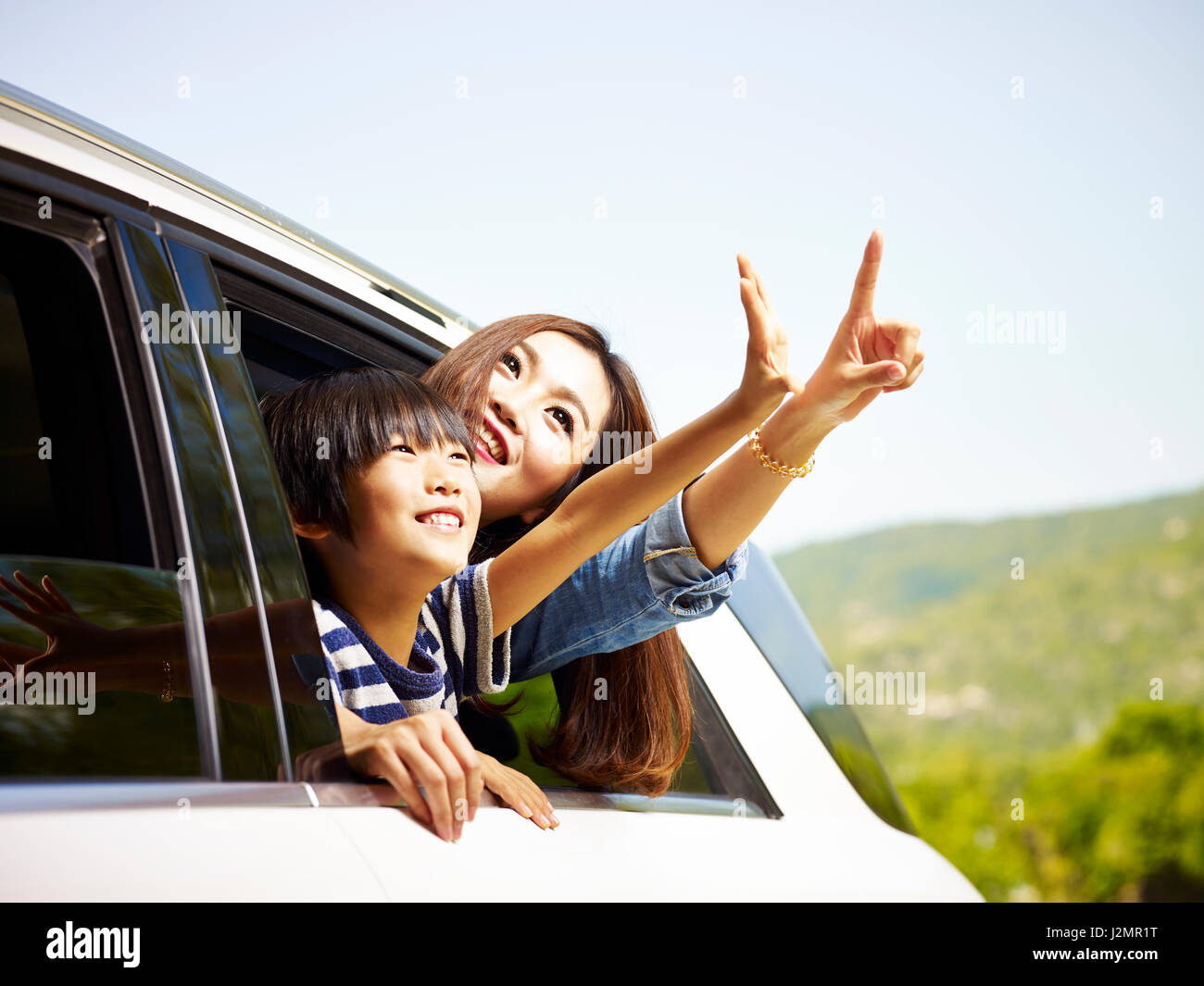 happy asian mother and son sticking heads out of rear window of a car looking at scenery. Stock Photo
