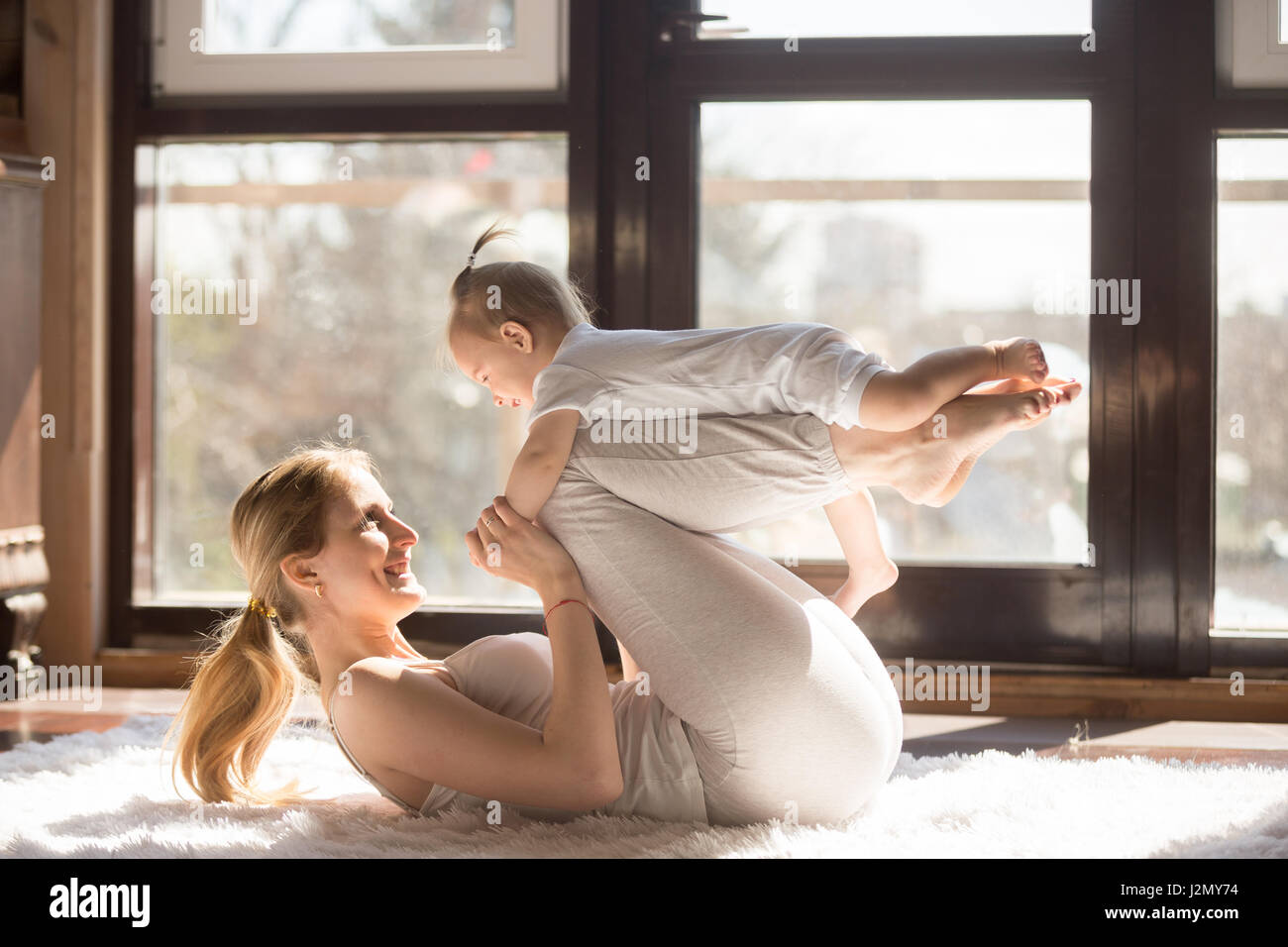 Young sporty mother and baby girl working out, exercising together at home, parent and child healthy development, game playing, fitness and relaxation Stock Photo
