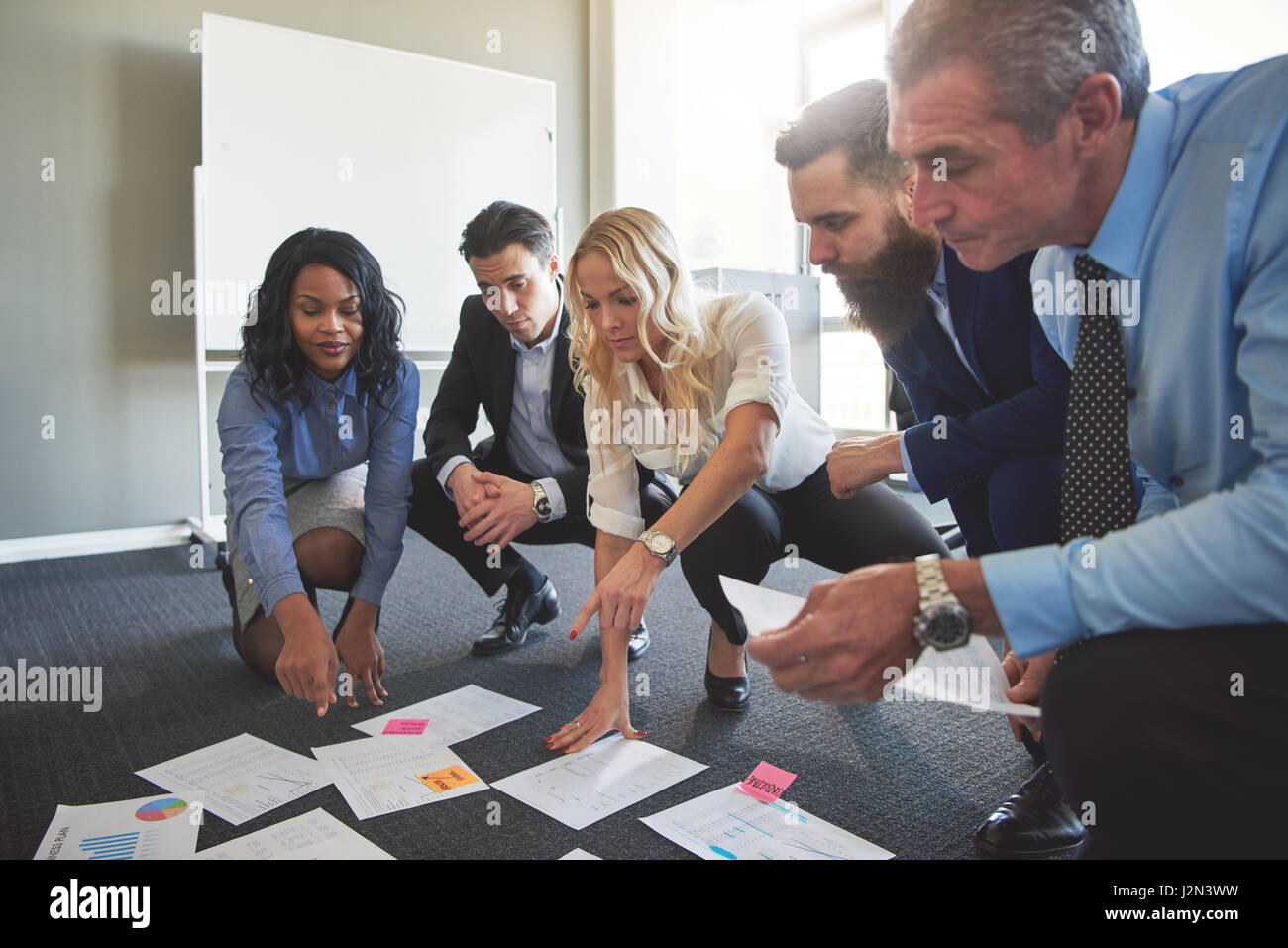 Men and woman brainstorming in office crouching to look at different documents Stock Photo