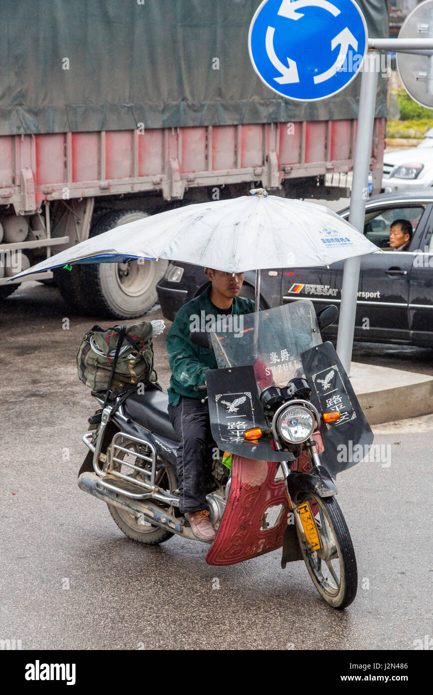 Kaili, Guizhou, China.  Young Man on Motorbike with Umbrella. Stock Photo