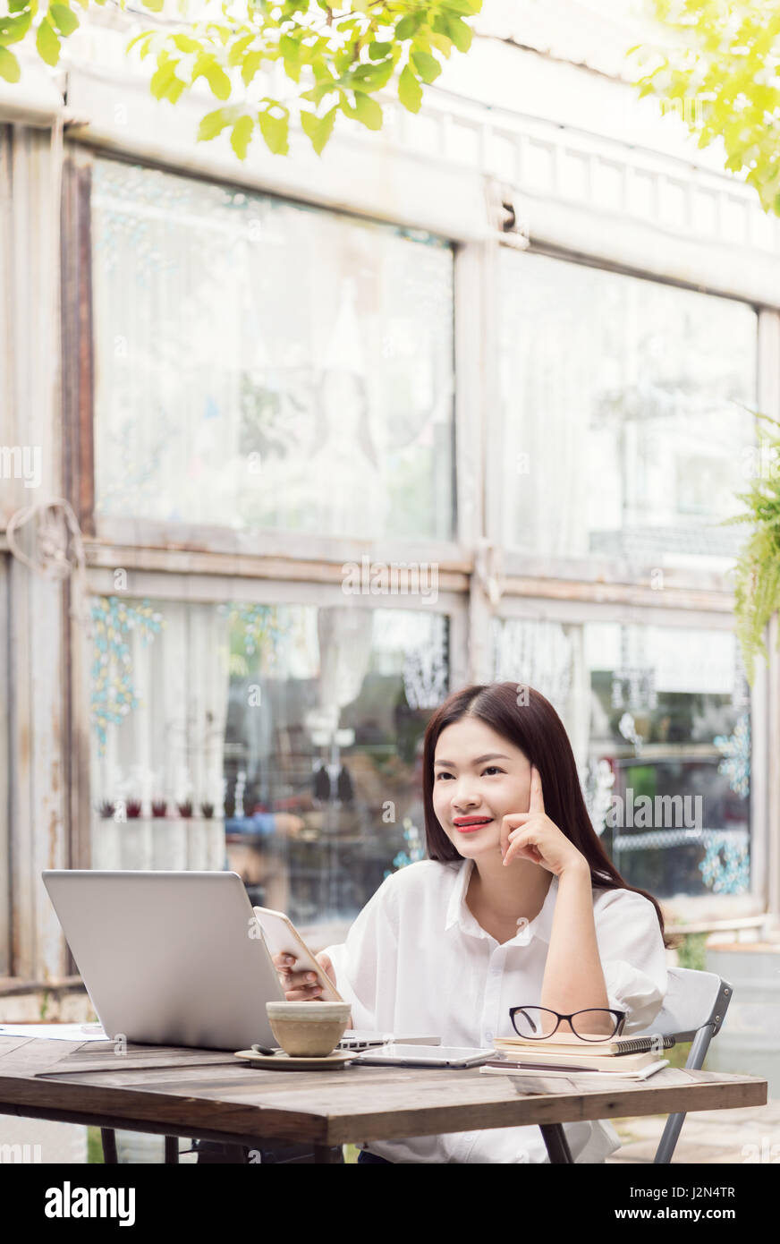 happy young asian woman thinking and enjoying her coffee while using ...