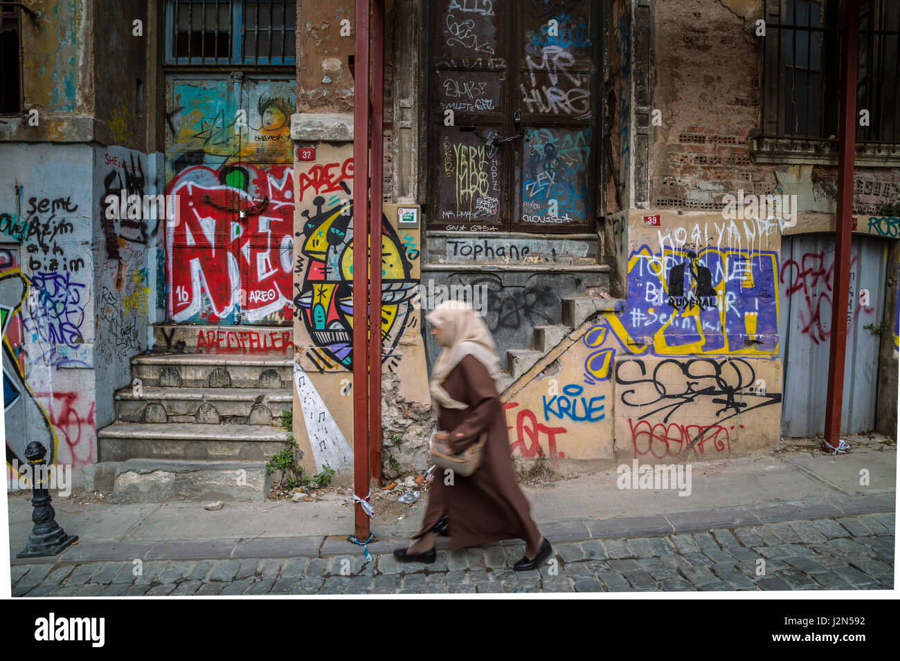 Building facade covered with graffiti in Galata area and a woman in a headscarf passing by, in Istanbul, Turkey Stock Photo