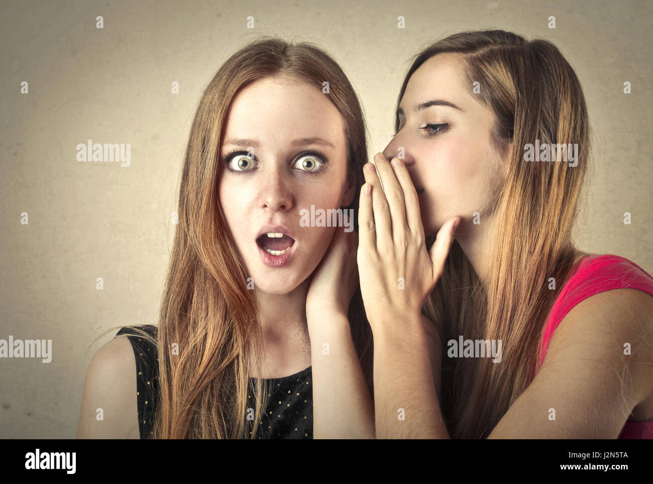 Woman whispering something to suprised woman Stock Photo